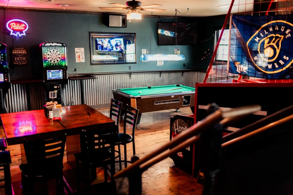 Dimly lit bar interior with a pool table, arcade games, and neon signs.