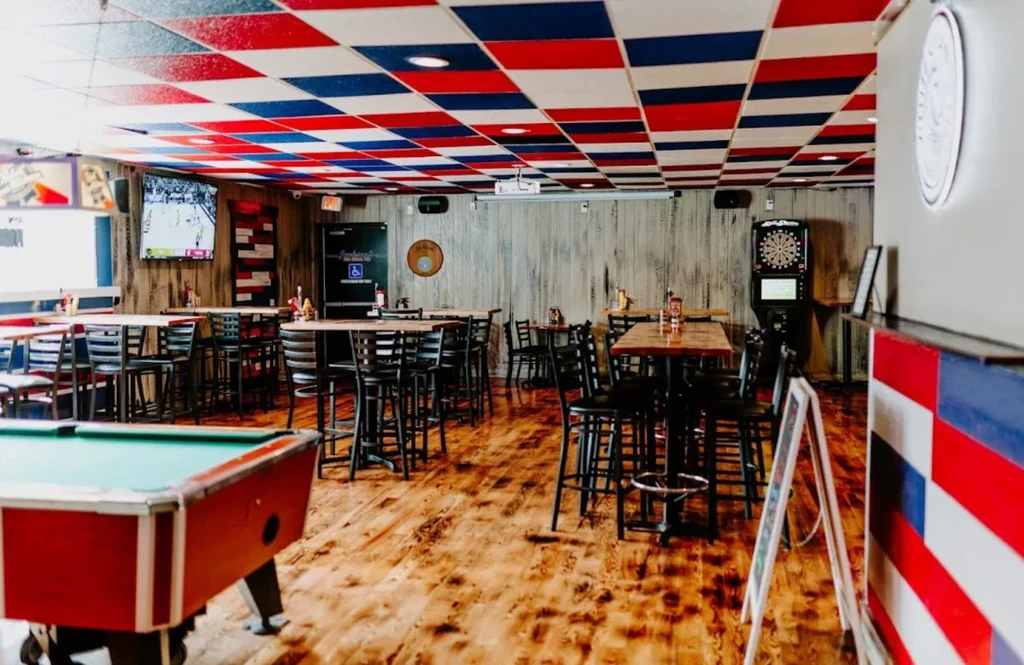 Empty casual sports bar with checkerboard ceiling, pool table, and dartboard.