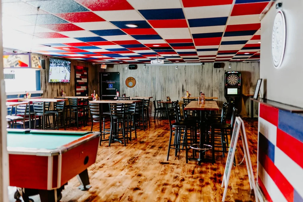 Patriotic-themed bar interior with checkerboard ceiling, pool table, and dartboard.