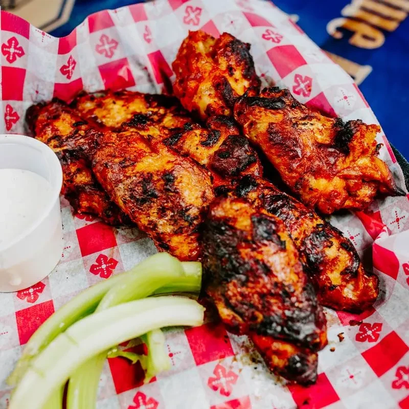 Sauced chicken wings with dip and celery in a checkered basket.