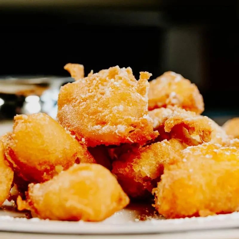Pile of golden-brown fritters dusted with powdered sugar on a plate.