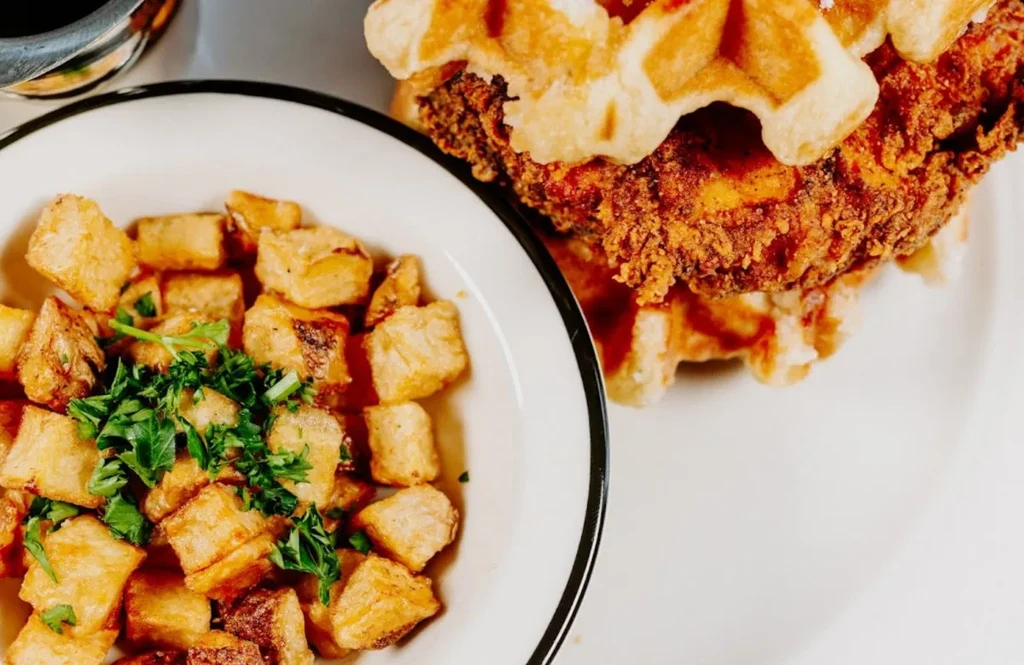 Chicken and waffles with a side of parsley-garnished roasted potatoes.