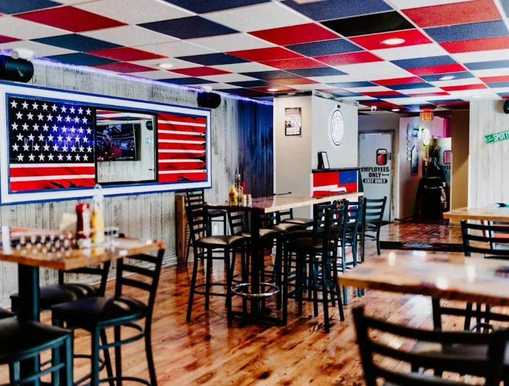 Casual American restaurant with flag TV, checkerboard ceiling, and high tables.