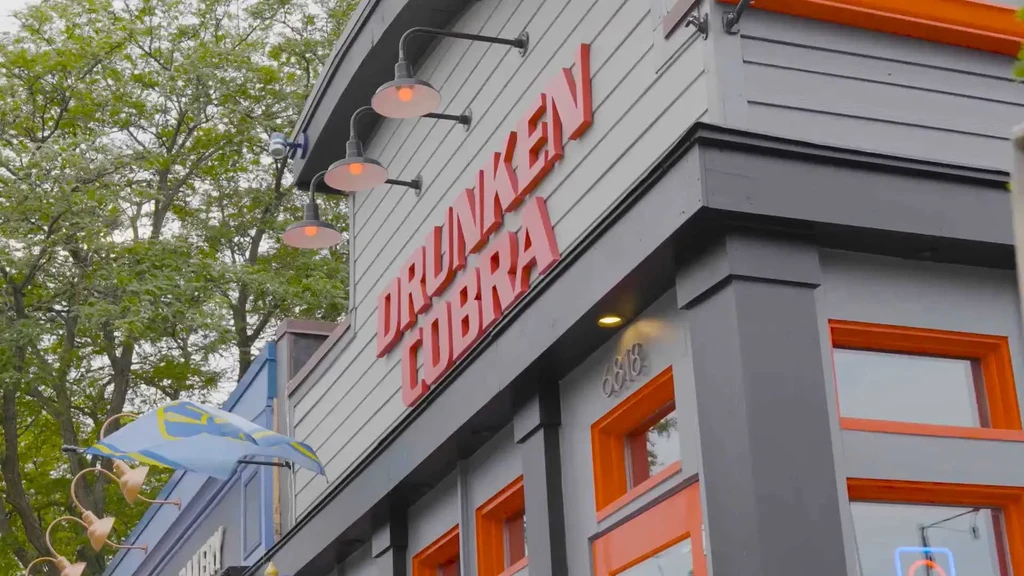 Building facade with 'DRUNKEN COBRA' sign, orange windows, green tree.