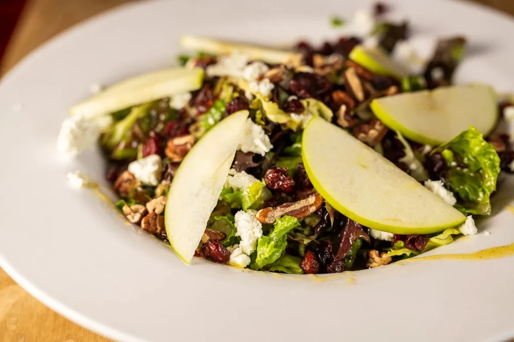 Vibrant salad with greens, apple, cheese, cranberries, and nuts.