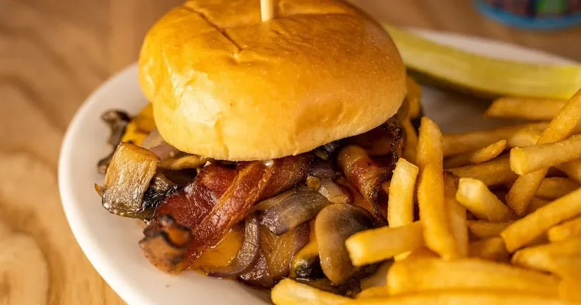 Brioche burger with bacon, mushrooms, onions, fries, and pickle.