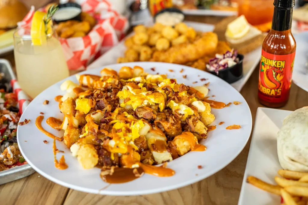 Tater tot poutine with eggs and bacon on a white plate, wooden table.