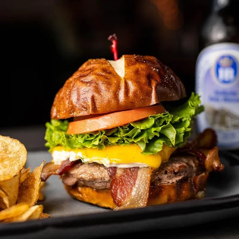 A gourmet burger, potato chips, and a blurred beer bottle.