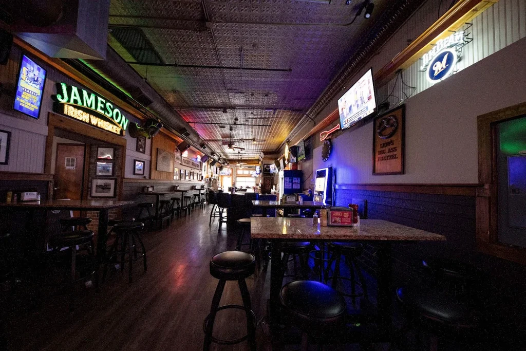 Dimly lit bar interior with dark wood, neon signs, and seating.