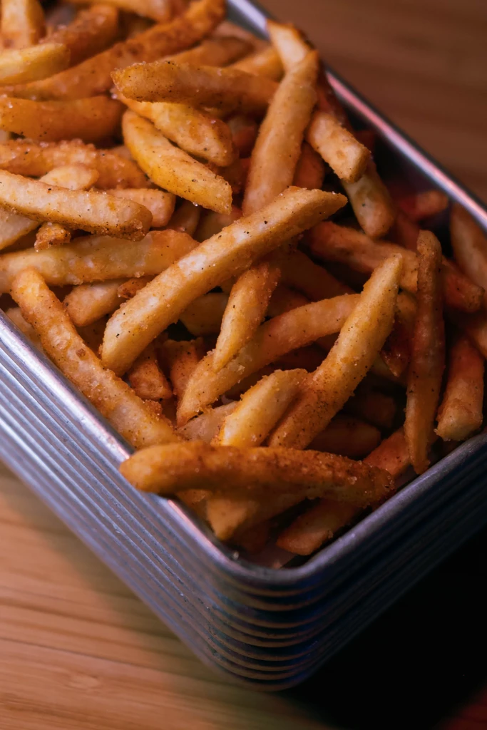 Golden-brown seasoned french fries piled high in a corrugated metal tray.
