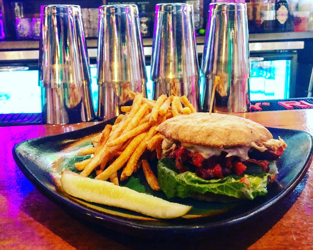 Substantial burger, fries, and pickle on a bar counter.