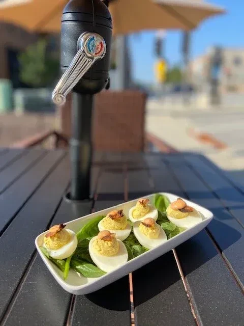 Six bacon deviled eggs on spinach, served on an outdoor table.
