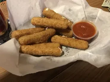 Golden-brown mozzarella sticks with oozing cheese, marinara, in a basket.