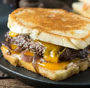 Sliced patty melt with melted cheese and caramelized onions on a dark surface.