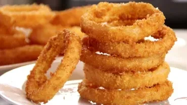 Several golden-brown, breaded onion rings stacked on a white plate.