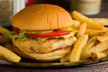 Close-up of a non-beef burger with lettuce, tomato, pickles, and fries.
