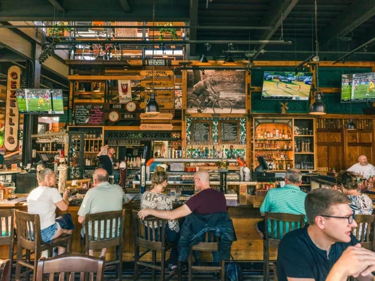 Lively industrial-chic bar with patrons, a bartender, and sports on TVs.
