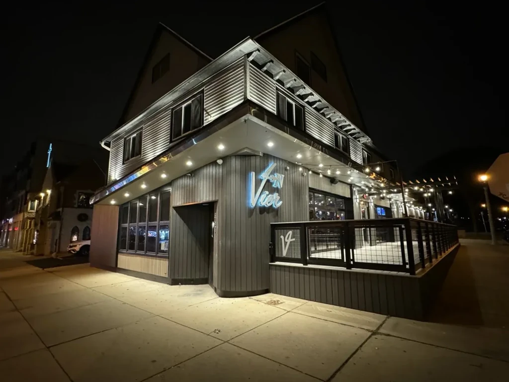 Modern building "Vier" with peaked roof, blue neon sign, lit patio.