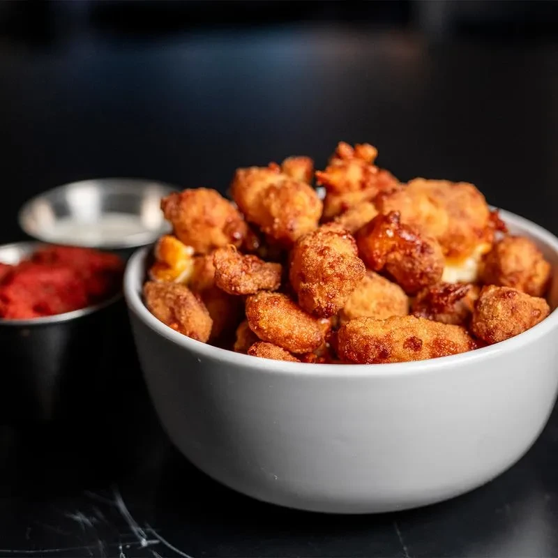 White bowl of golden fried food with red and white dipping sauces.