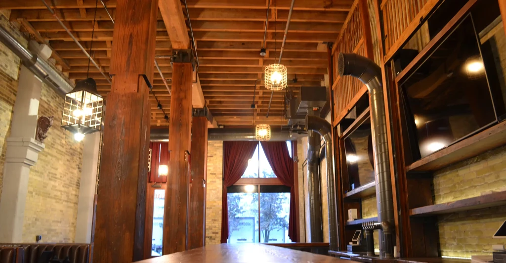 Rustic industrial-chic restaurant interior with wood beams, brick walls, and lanterns.