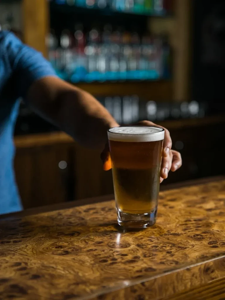 Frothy amber beer glass on a burl wood bar, hand reaching.