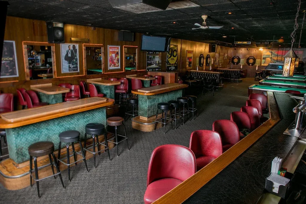 Dimly lit pub interior with wood walls, pool tables, and various seating.