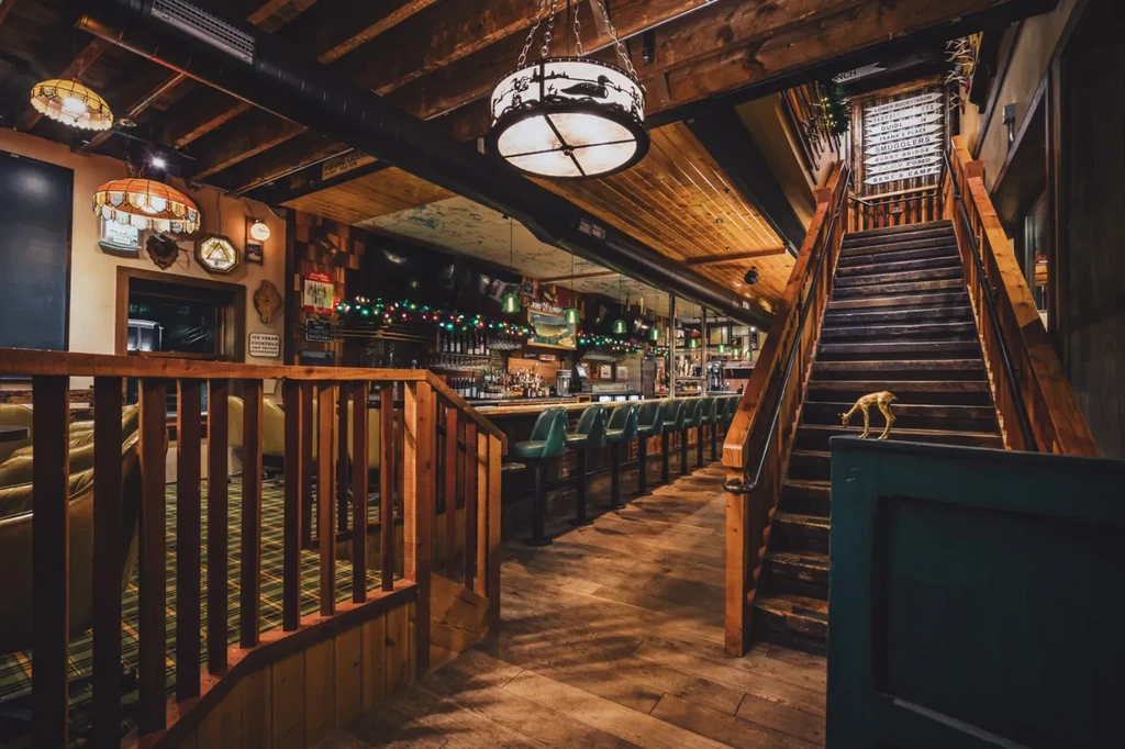 Rustic wooden restaurant interior with a bar, staircase, and lodge decor.