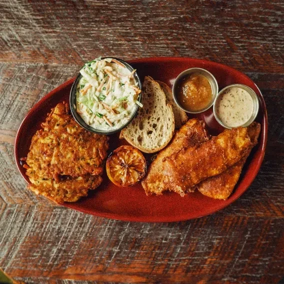 Plate of fried fish, fritters, coleslaw, bread, and dipping sauces.