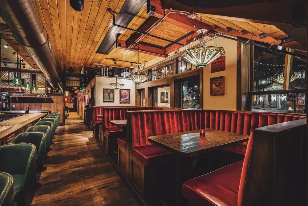 Warm industrial restaurant interior, wooden bar, green stools, red booths.
