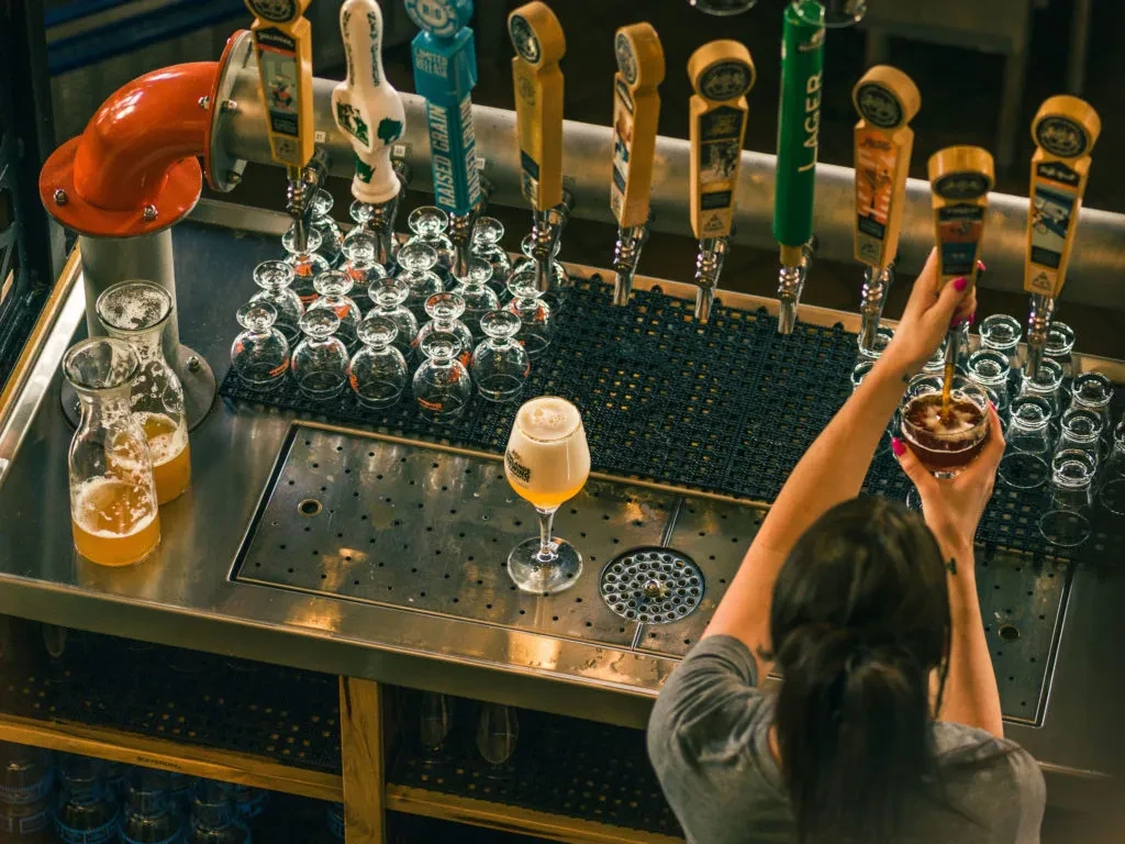 Overhead shot of bar counter with beer taps, glasses, person pouring.