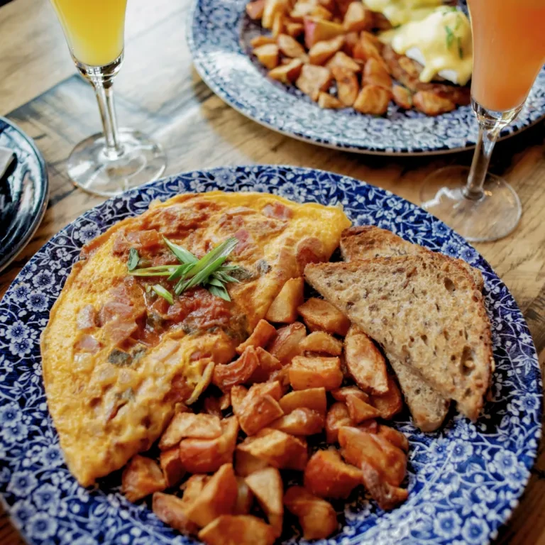 Omelet, home fries, and toast on a patterned plate, wooden table.