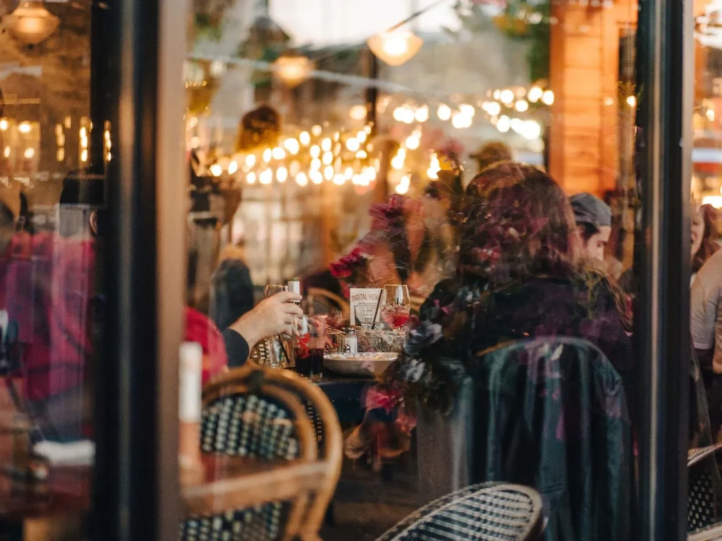 Cozy restaurant patrons seen through a window with warm light reflections.
