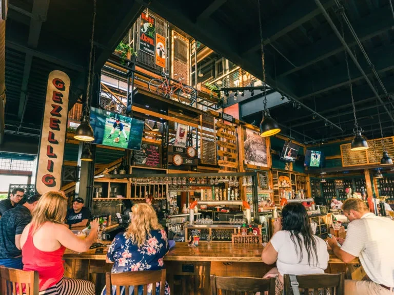 Lively rustic-industrial bar interior with patrons, TVs, and vintage decor.