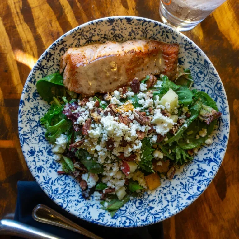 Pan-seared salmon, green salad, feta, pecans, fruit on a decorative plate.