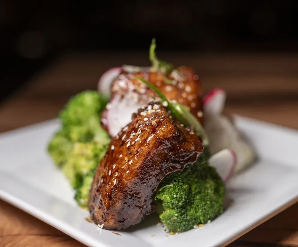 Glazed meat with dark sauce, sesame seeds, broccoli, and radishes.