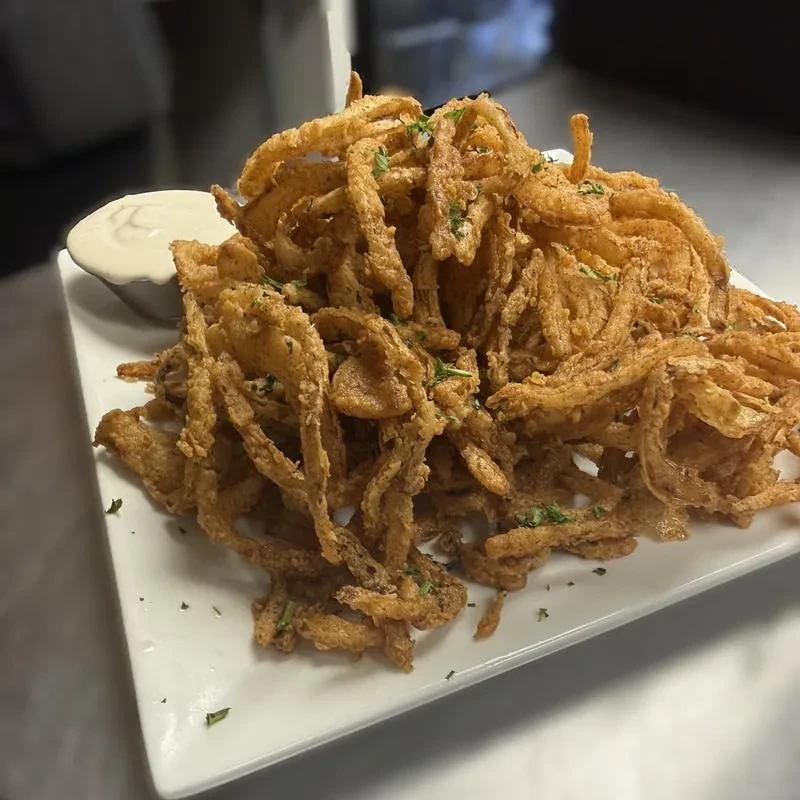 Crispy golden fried onion straws with green herbs and dipping sauce.