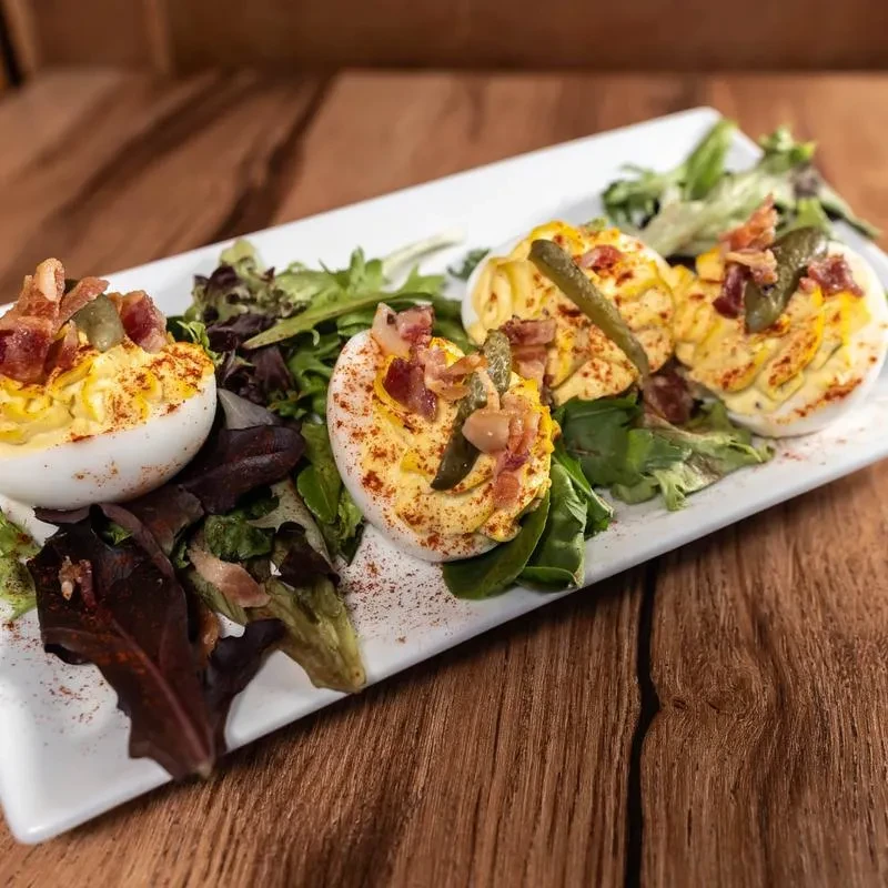Close-up of four deviled eggs topped with bacon, pickles, paprika.