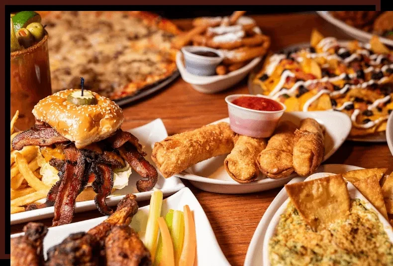 Table of comfort foods: burger, fries, nachos, pizza, and egg rolls.