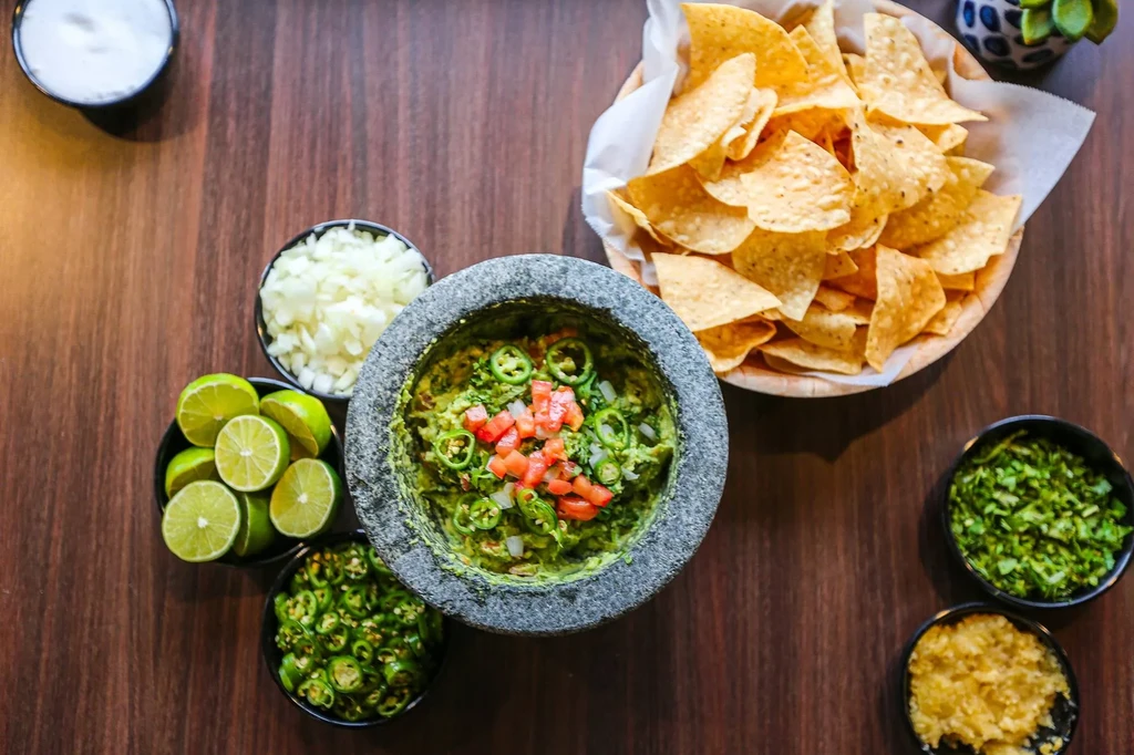 Guacamole in molcajete, surrounded by fresh ingredients and tortilla chips.