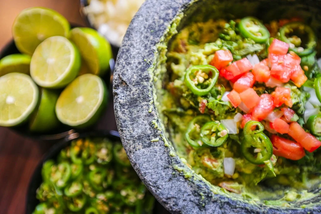 Fresh guacamole in molcajete, topped with tomatoes, jalapeños, and limes.