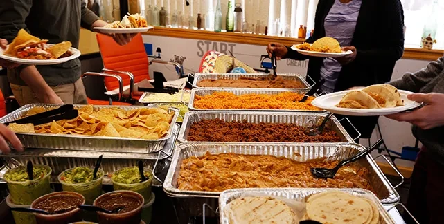 People serving varied Mexican and Tex-Mex dishes from a buffet.