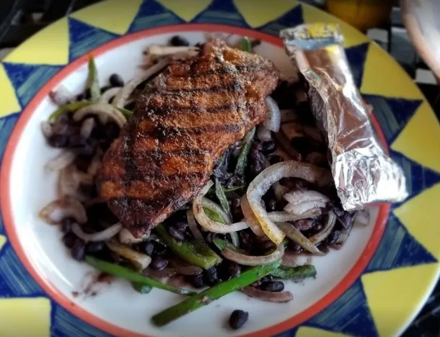 Plate of grilled meat, black beans, peppers, onions, and foil packet.