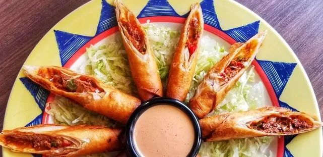 Six deep-fried meat-filled rolls with sauce on a vibrant colorful plate.