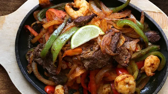 Sizzling beef and shrimp fajitas with peppers, onions, and lime.