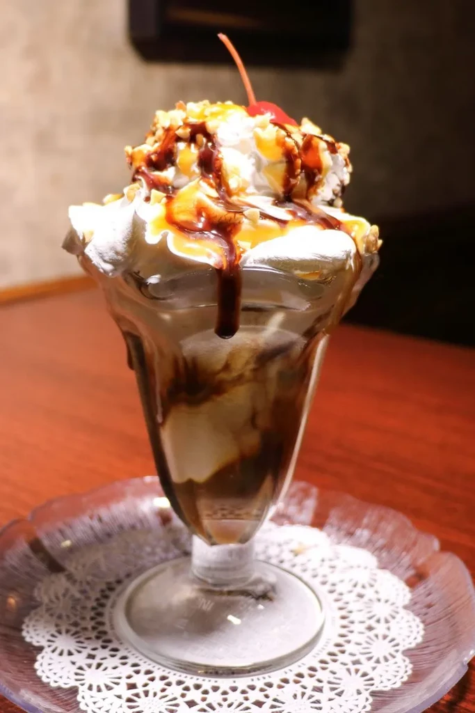 Sundae in tall glass with whipped cream, sauces, nuts, and cherry.