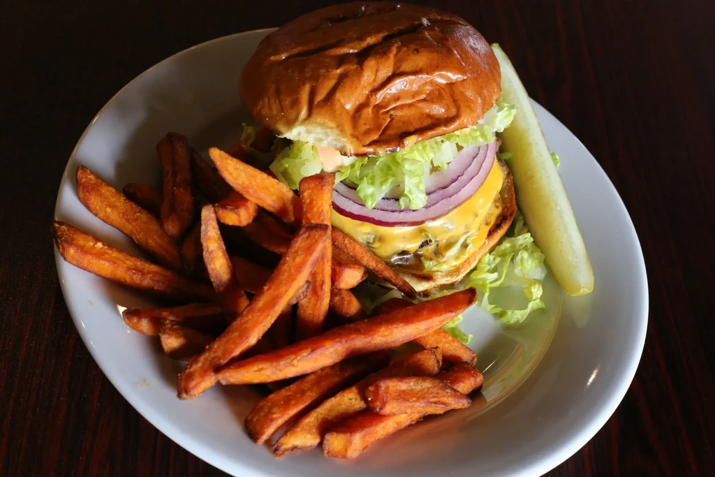 A cheeseburger, sweet potato fries, and a pickle on a white plate.