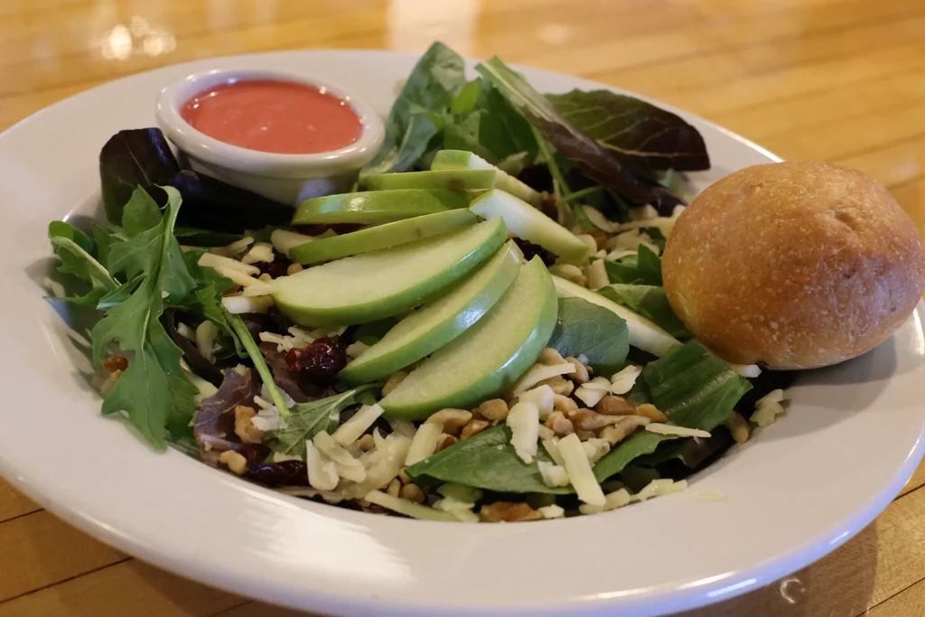 Salad with mixed greens, apples, cranberries, nuts, cheese, dressing, and roll.