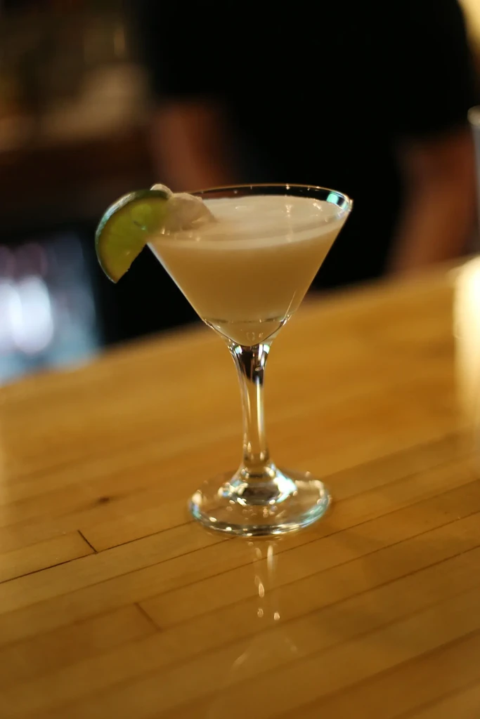 Creamy cocktail in martini glass with lime on a wooden bar.