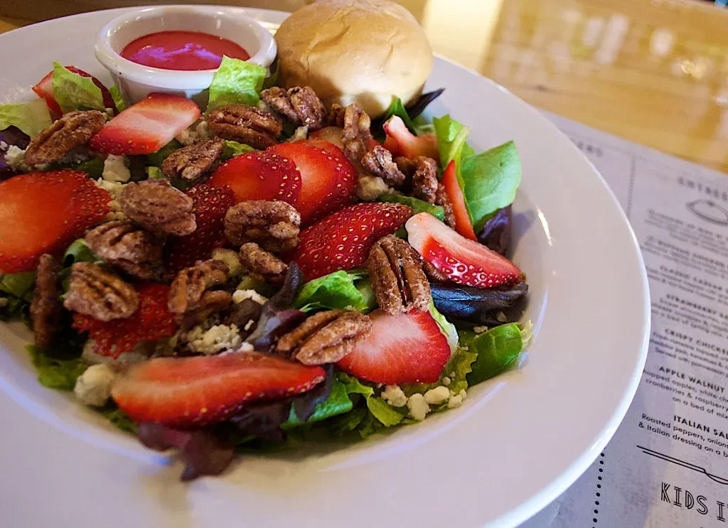 Strawberry pecan salad on a white plate with dressing and bread.