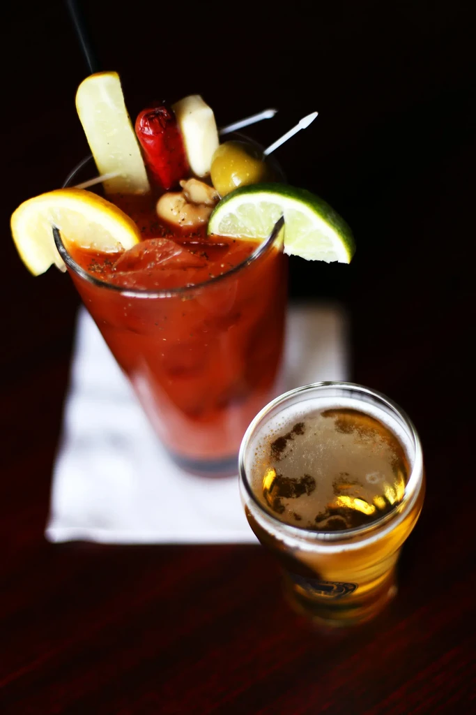 Heavily garnished Bloody Mary and a golden beer on a dark surface.